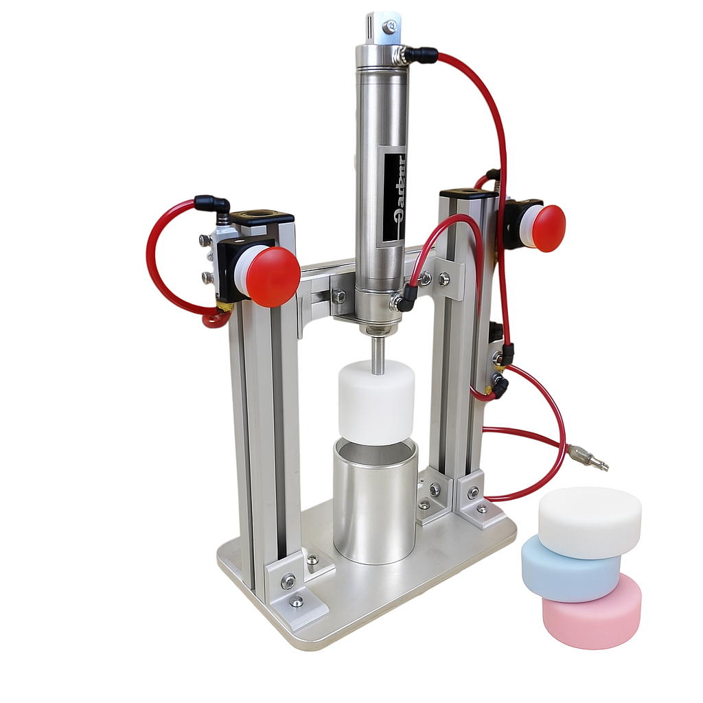 “Pneumatic shampoo bar press machine made of aluminum with red air hoses, pressing a round shampoo bar mold. Beside the press, three finished shampoo bars in white, light blue, and light pink are stacked neatly.